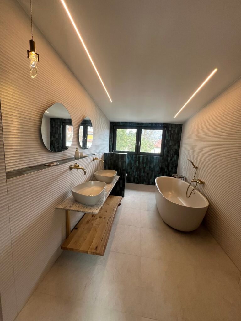 Modernes Badezimmer nach Badsanierung mit freistehender Wanne, Doppelwaschtischen, Holzablage und Fliesenarbeiten