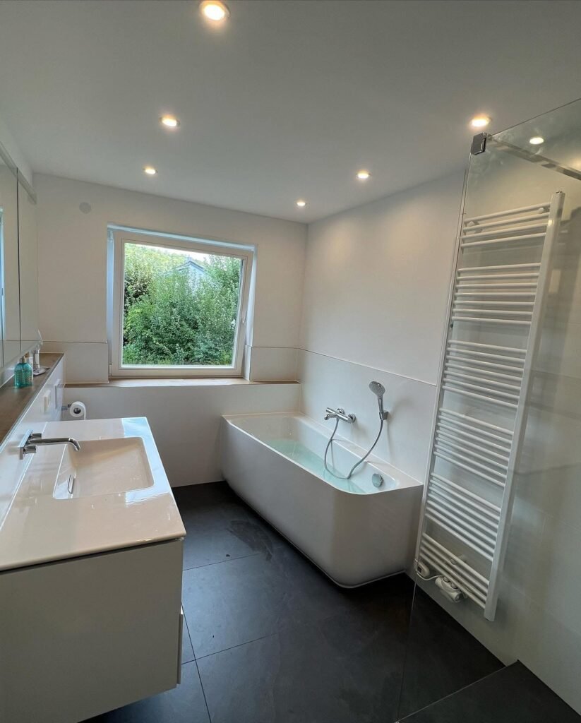 Modernes Bad mit freistehender Wanne, Waschtisch, Handtuchheizung und dunklen Fliesen, Badsanierung